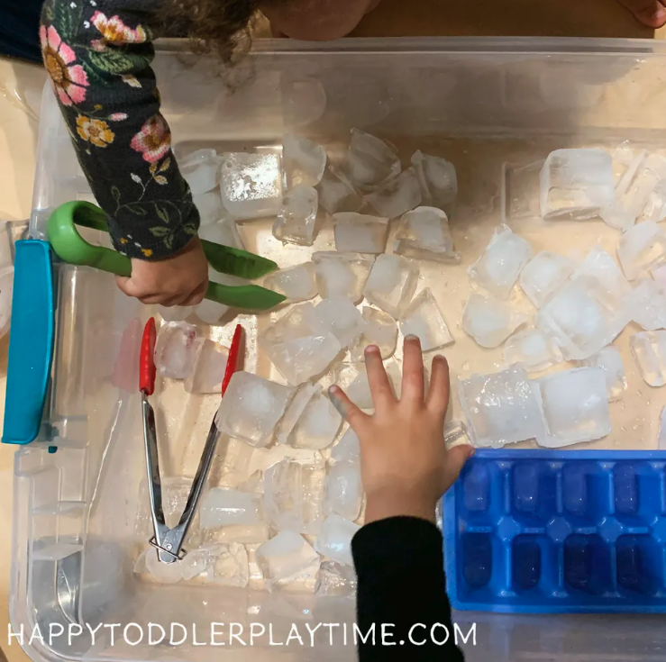 Toddlers playing in a sensory ice bin with tongs. 