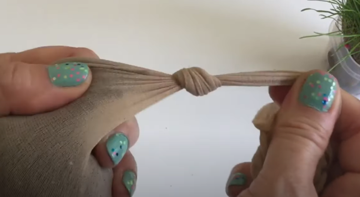 Tights with soil and seeds in it and a pair of hands tying a knot in it for a fun Science project. 