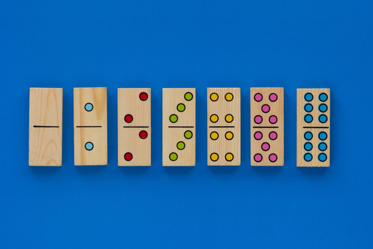 A row of wood dominos numbered 0 to 12  with colorful dots on a blue back ground. 