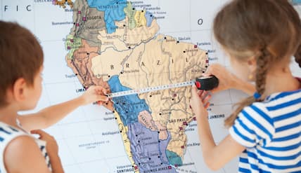 Kids using a measuring tape to measure a map. 