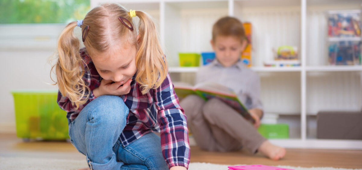 Girl looking at sight word matching cards. Boy in the background reading.  