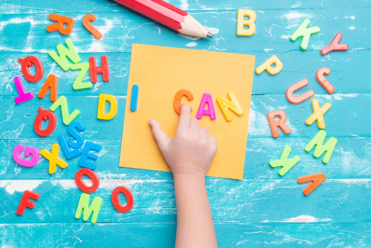 Magnetic alphabet letters on a table with a finger pointing to the words I can. 