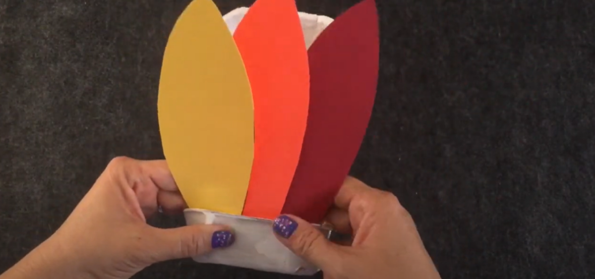 Gluing colorful paper feathers into an egg carton for a Thanksgiving turkey craft. 