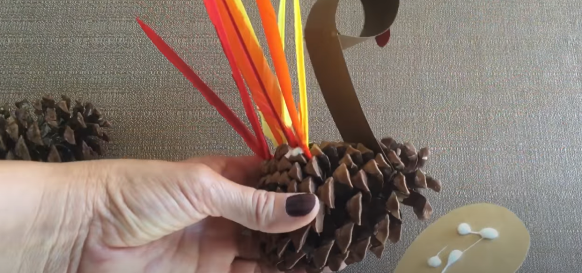 Adding the long strip of paper to a pinecone for a Thanksgiving turkey craft. 