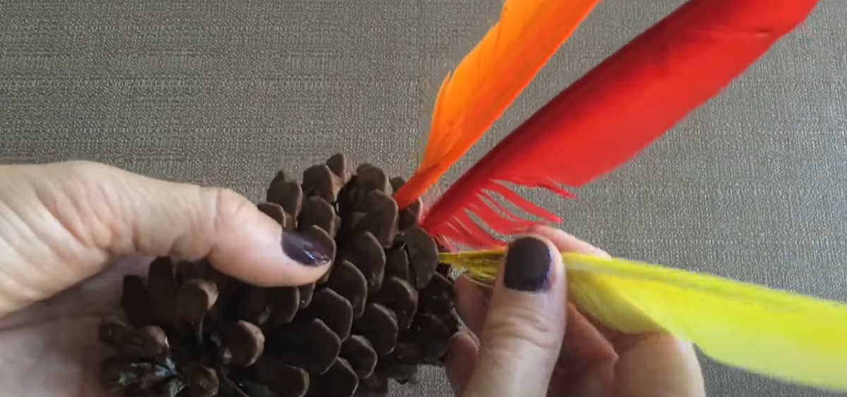 Adding feathers to a pinecone to create a Thanksgiving turkey craft. 