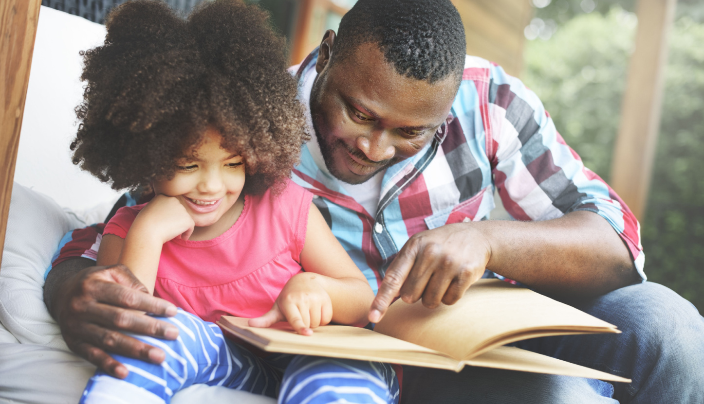 Father point to the words in a book while reading to his daughter. 