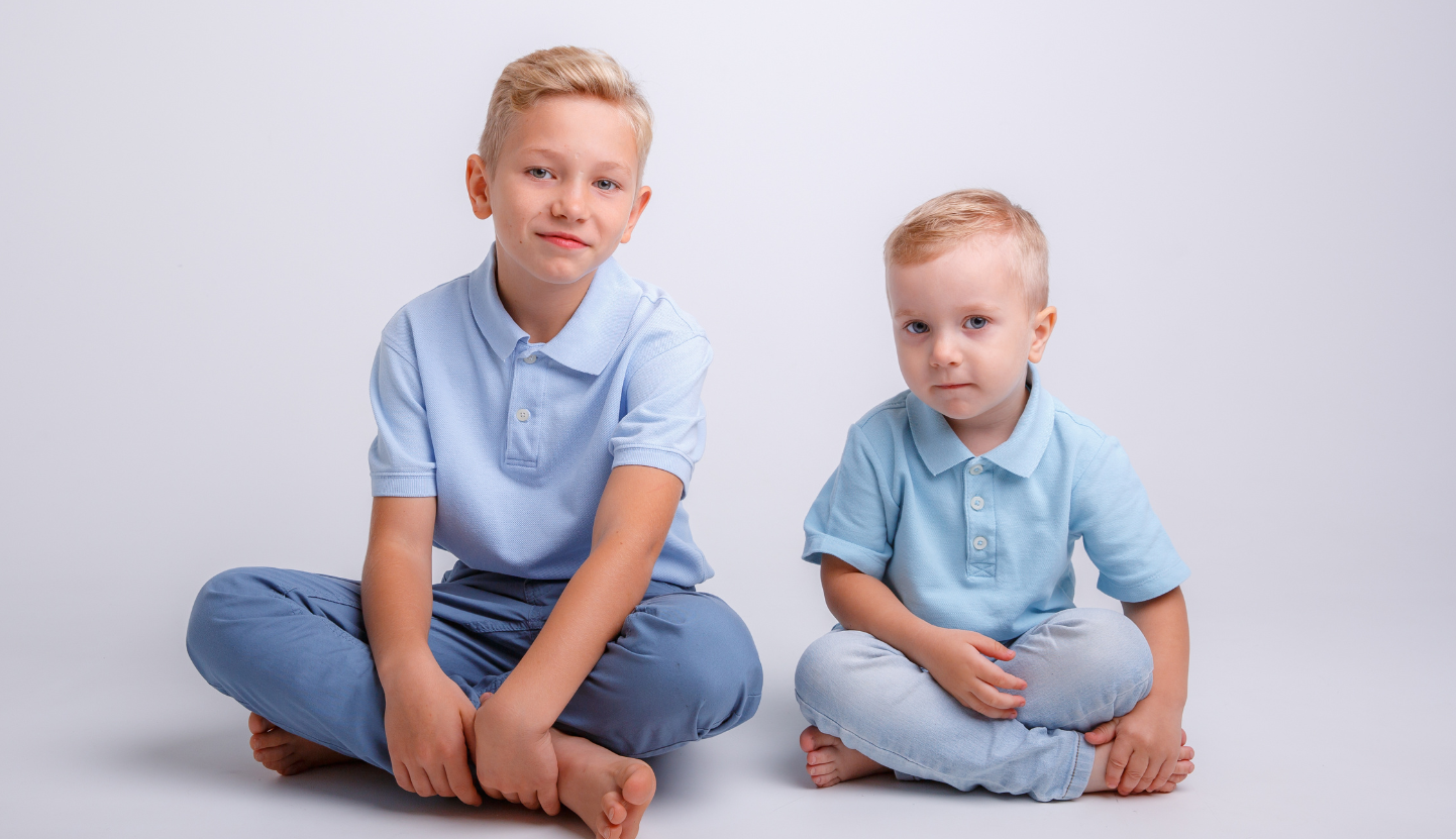 Two boys different ages in blue shirts sitting next to each other. 