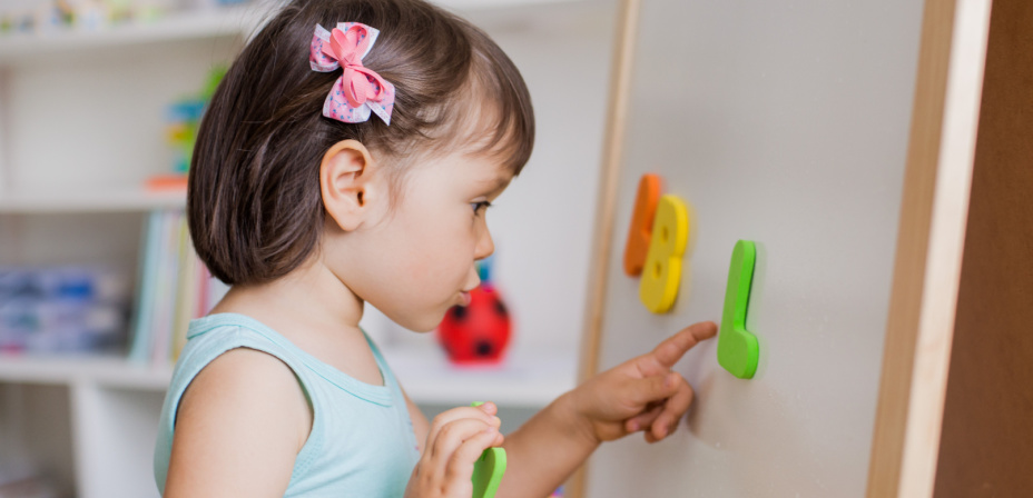 A young girl looking at colorful letters on a white board. 