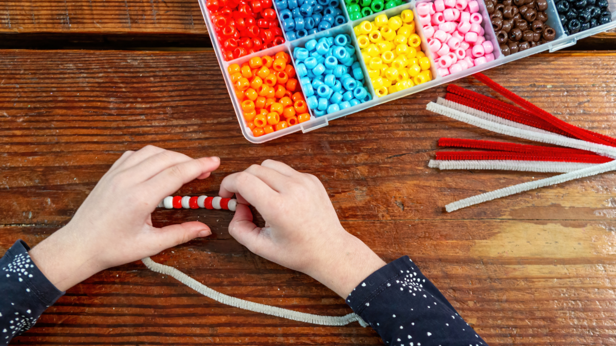 A preschooler putting colorful beads onto a pipe cleaner. 