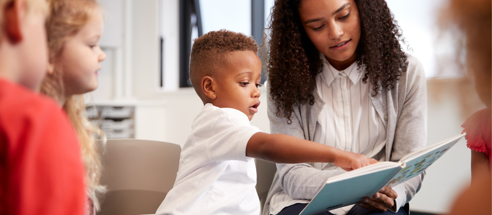 Child pointing to a book and reading with his teacher. 