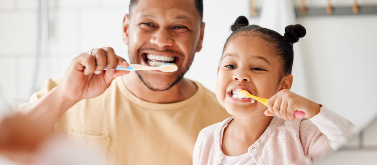 Dad and daughter brushing their teeth together. 