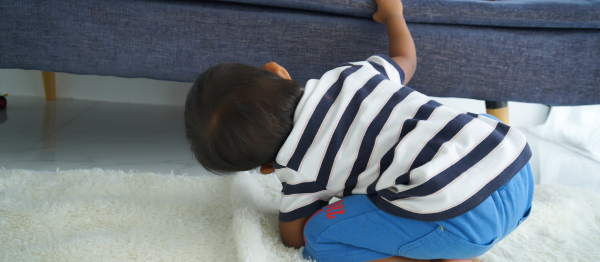 Boy looking for letters under a couch. 