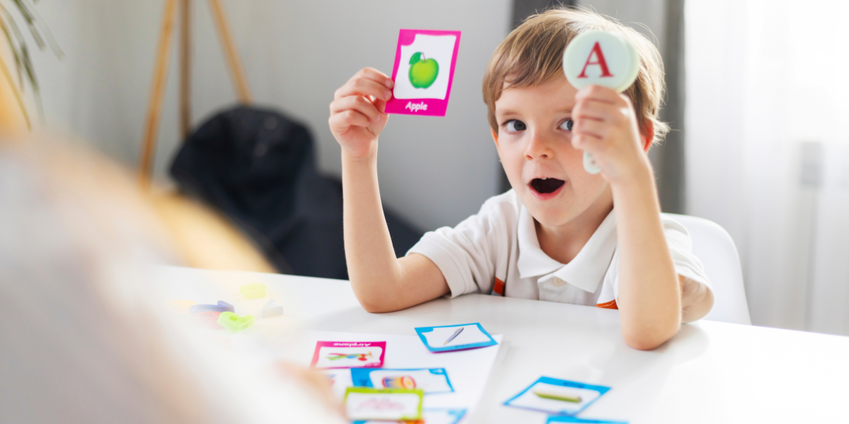 A young boy holding up the letter A and a picture of an apple. 