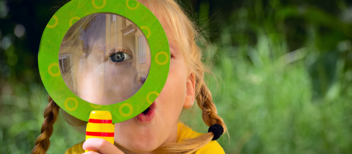 Young girl with a surprised face looking through a brightly colored magnifying glass. 