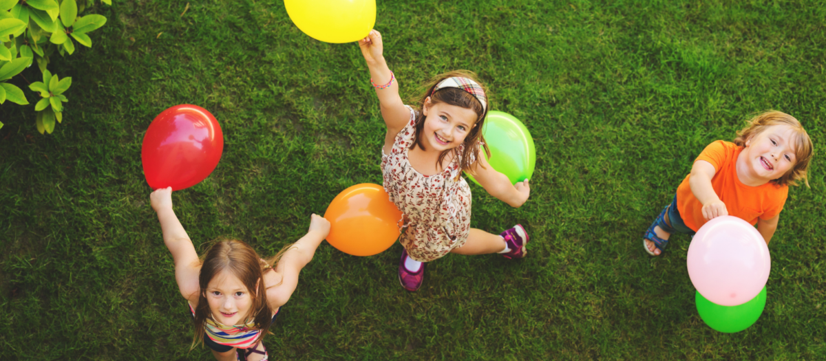 A group of young children outside playing with colorful balloons. 