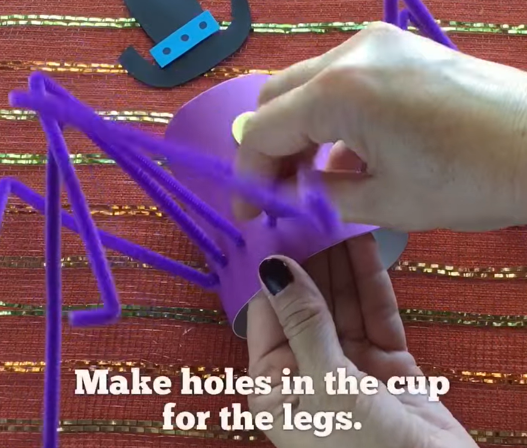 Putting the pipe cleaner legs in the spider craft by making holes in the cup for the legs. 