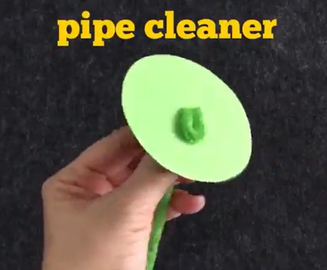 Looping pipe cleaner through a hole in the green construction paper circle. 