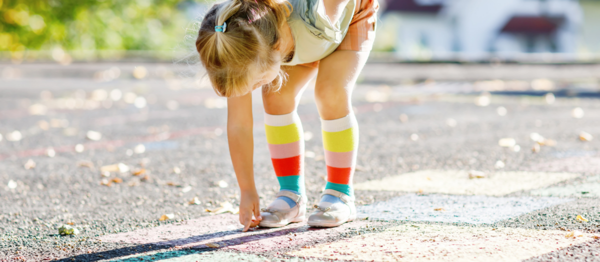 Girl leaning down and counting the numbers written in chalk. 