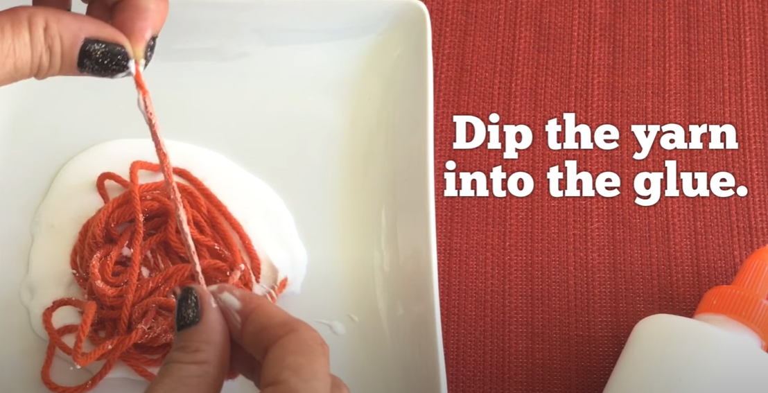 Dipping yarn into glue for a pumpkin yarn craft. 