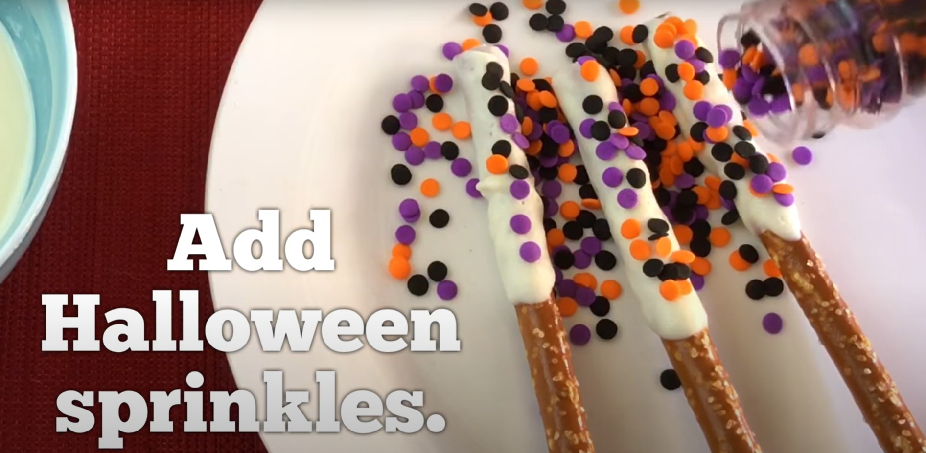 Colorful Halloween sprinkles being added to chocolate covered pretzels. 