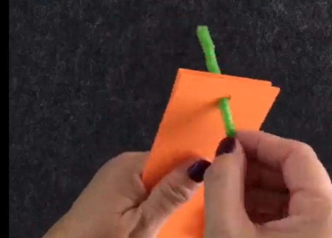 Pushing pipe cleaner through the holes in the ends of the orange construction paper strips. 