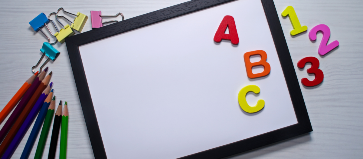 Colorful letters on a white board surrounded by color pencils. 