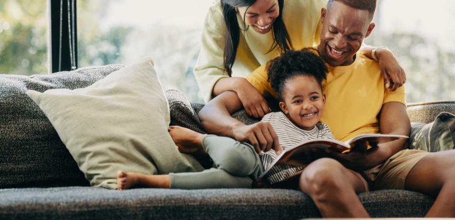 A young family reading a book together while sitting on the couch. 