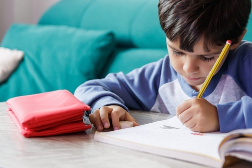 A young boy writing in a book with a pencil. 