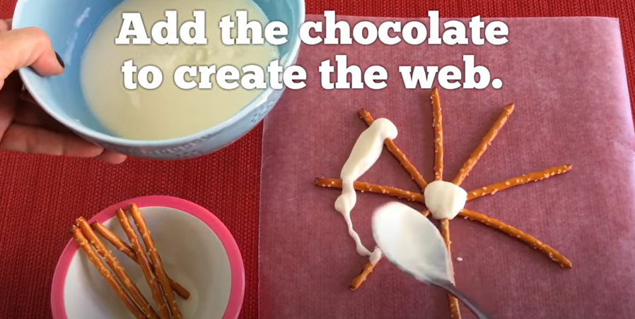 Small pretzels arranged in a web shape with white chocolate being drizzled. 