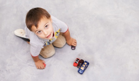 A small boy looking up from his toy cars on the floor. 