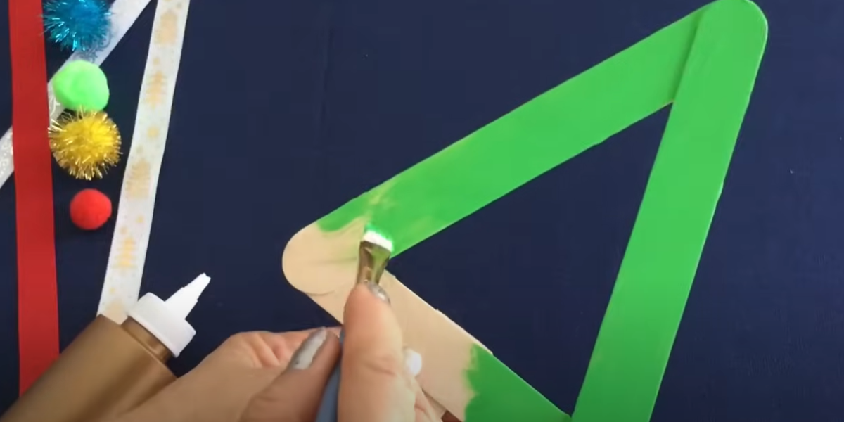 Painting the sticks bright green for this holiday ornament craft. 