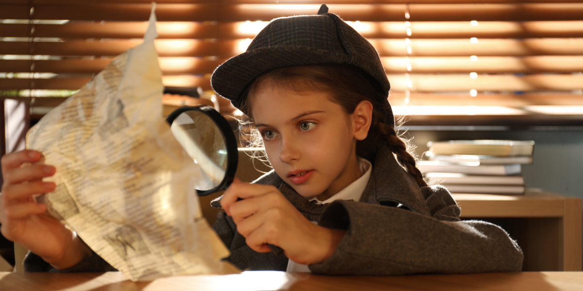 Young girl detective holding a magnifying glass to a paper. 