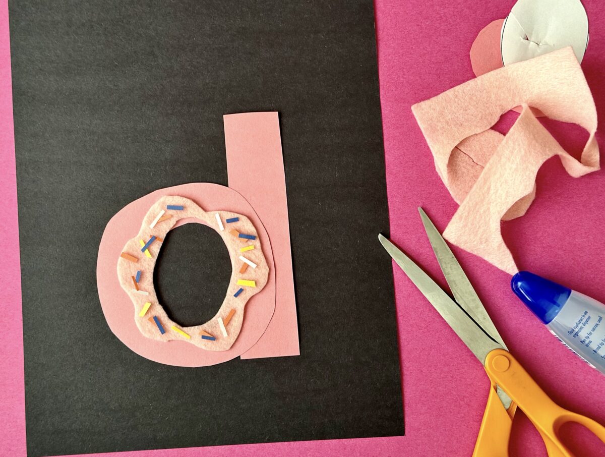 A pink letter d in the shape of a donut on a black piece of paper. 