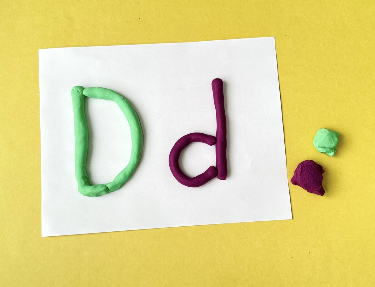 Green and purple playdough in the shape of an upper case letter D and lower case letter d, on a piece of white paper. 