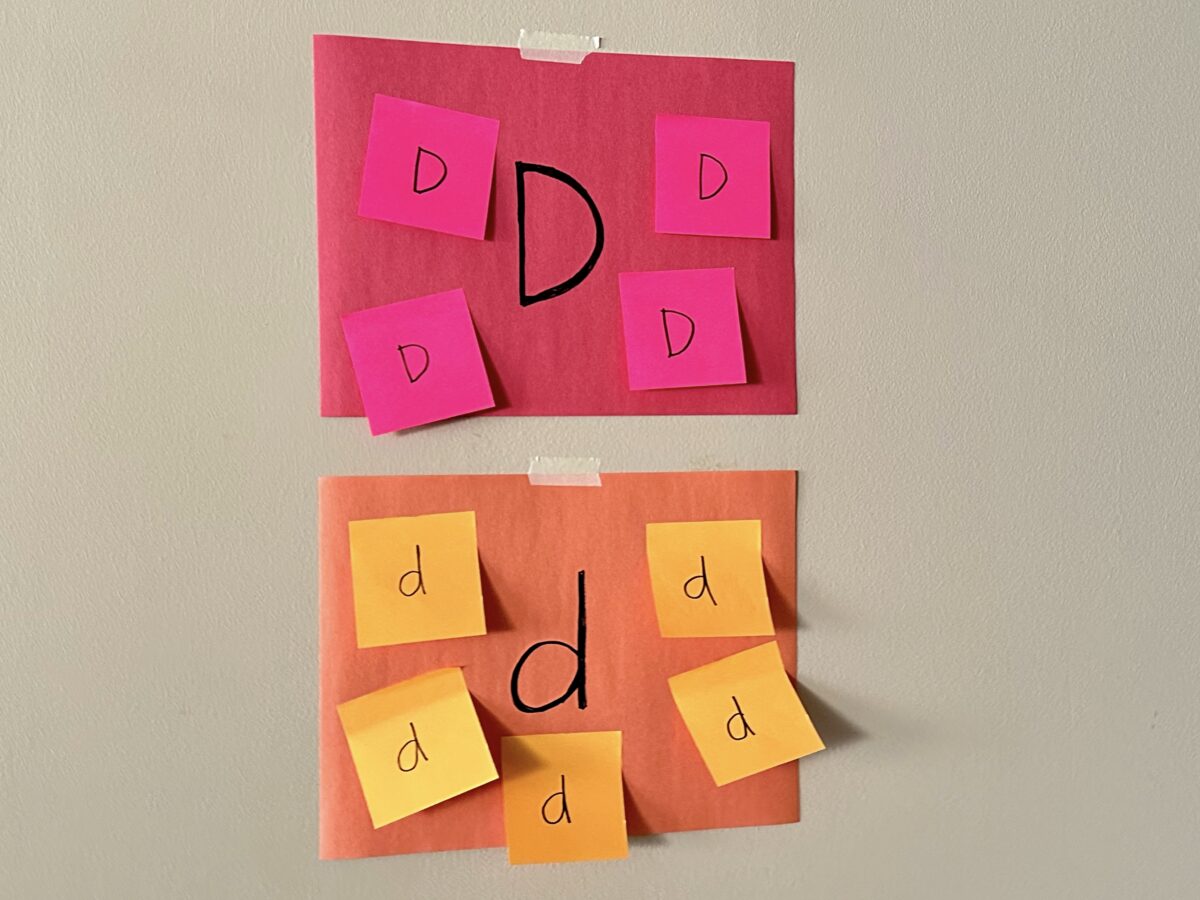 Colorful construction paper taped to the wall with sticky note letter d's stuck to them. 