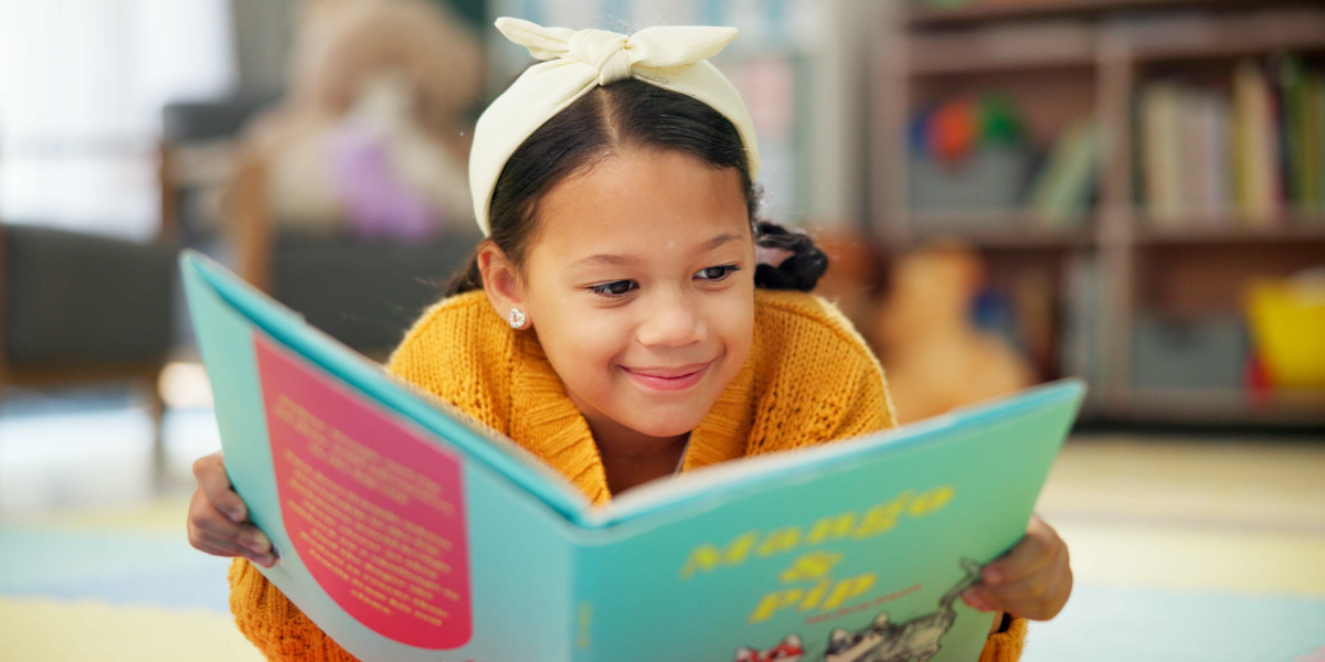 Young girl happily reading a book in the library. 