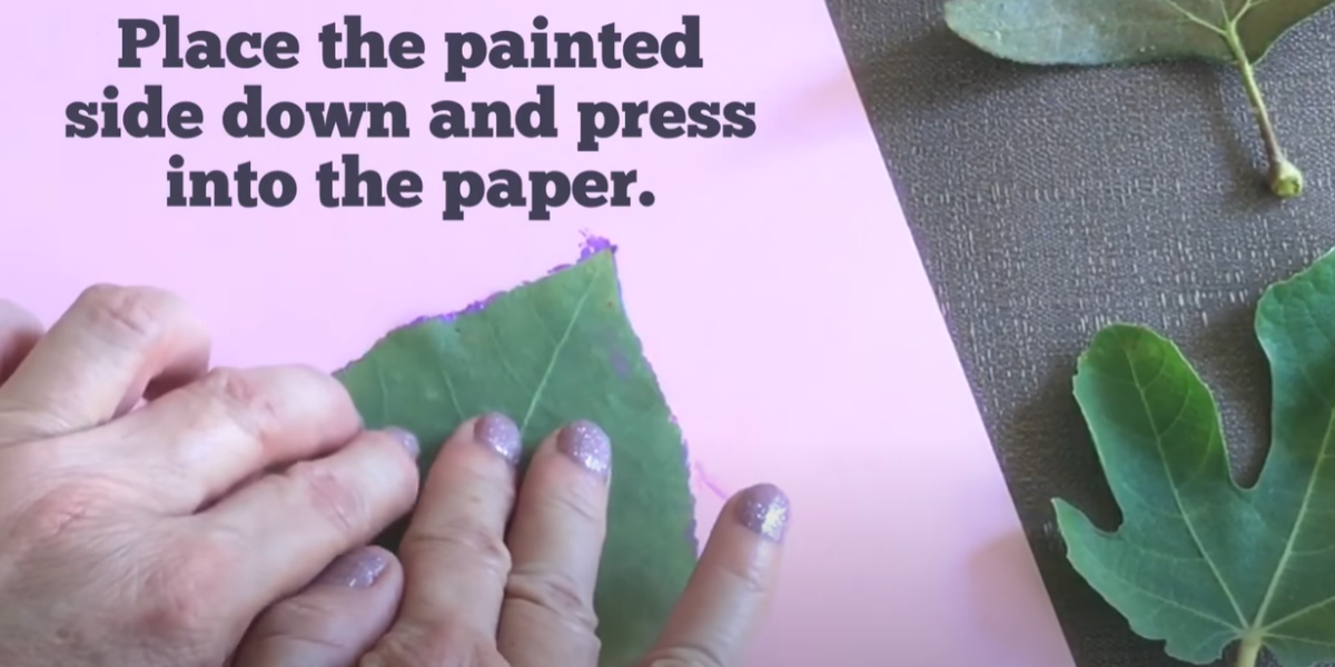 Placing a painted leaf paint side down on a piece of paper to create a print. 