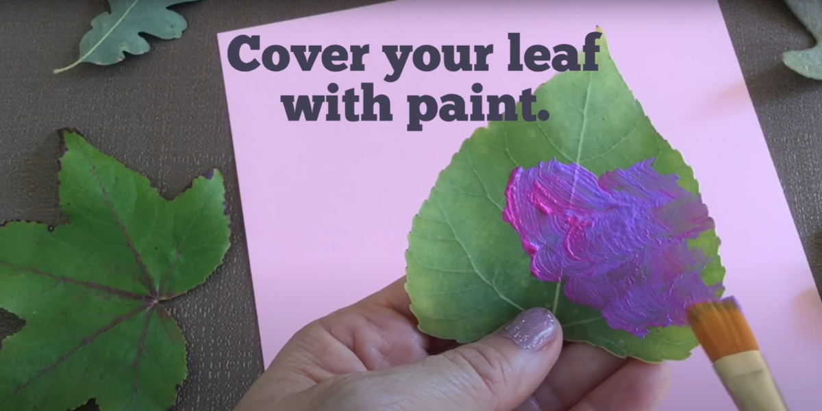 Painting a green leaf with purple paint. 