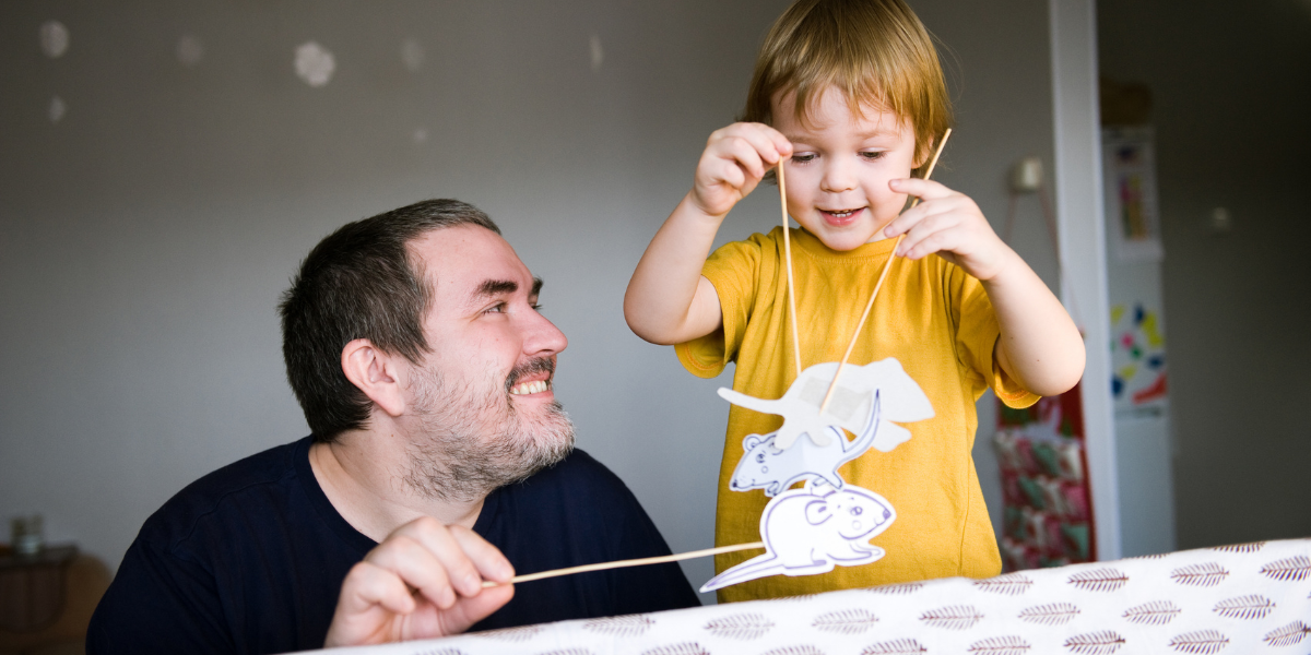 Father and son playing with paper puppet characters from a book. 