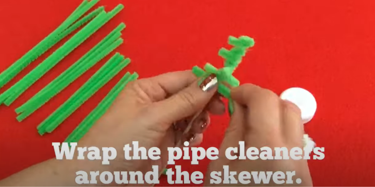 Wrapping green pipe cleaners onto a wooden skewer to create a fun pip cleaner Christmas tree craft. 