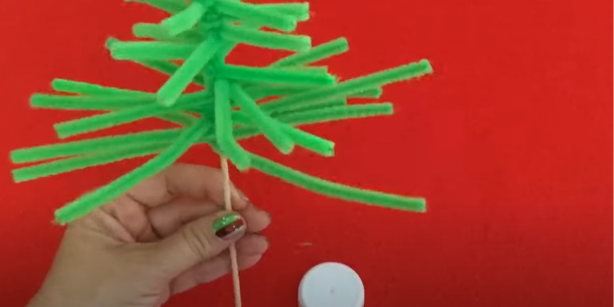 A hand holding a green pipe cleaner Christmas tree craft. 