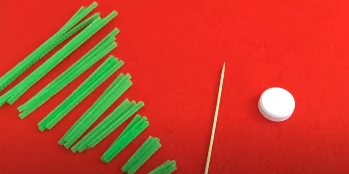 Green pipe cleaners, a white cap, and a wooden skewer on a red background. 