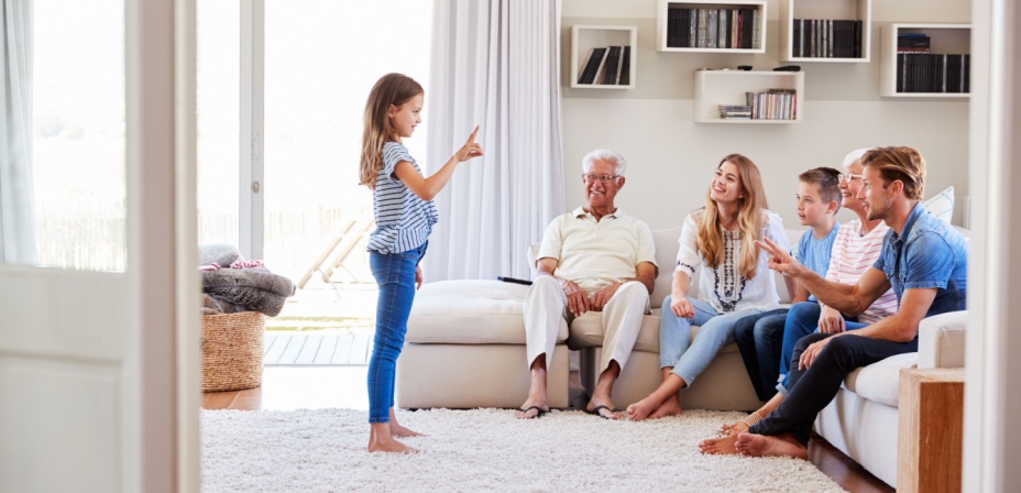 A young girl playing charades in the living room with her family. 