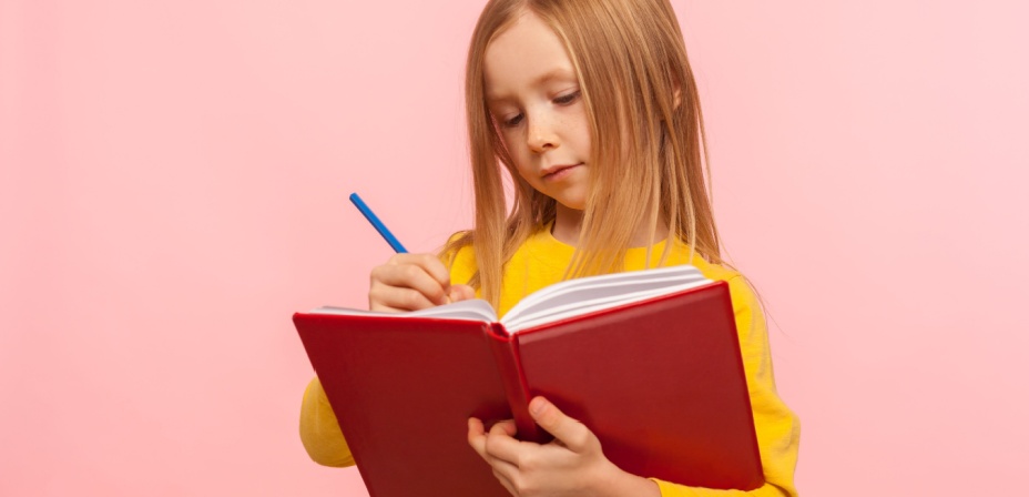 Young girl looking intently at a book while holding a pen in her hand. 