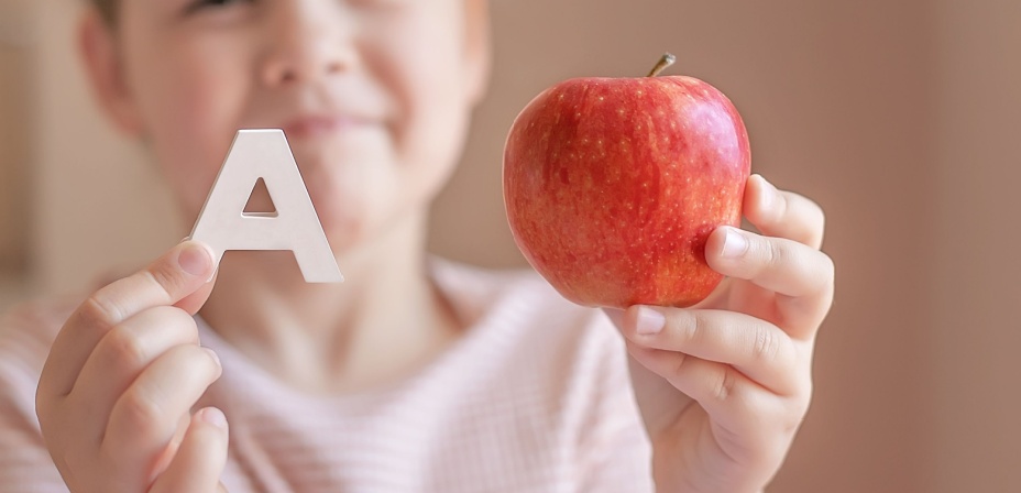 A child holding the letter A in one hand and an apple in the other. 