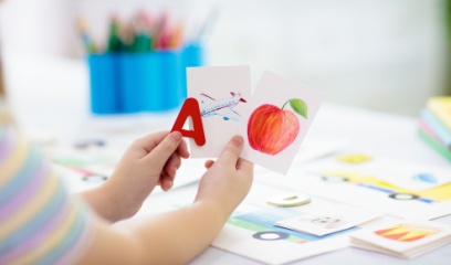 A child holding a red letter a in one hand and flashcards of an airplane in and apple in the other hand. 