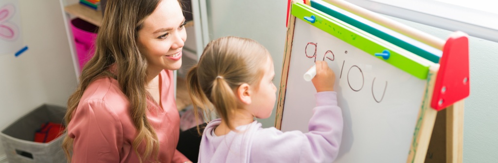 A teacher helping a child learn the vowels in the alphabet. 