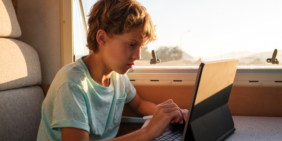 A boy doing computer work on a laptop from an RV. 