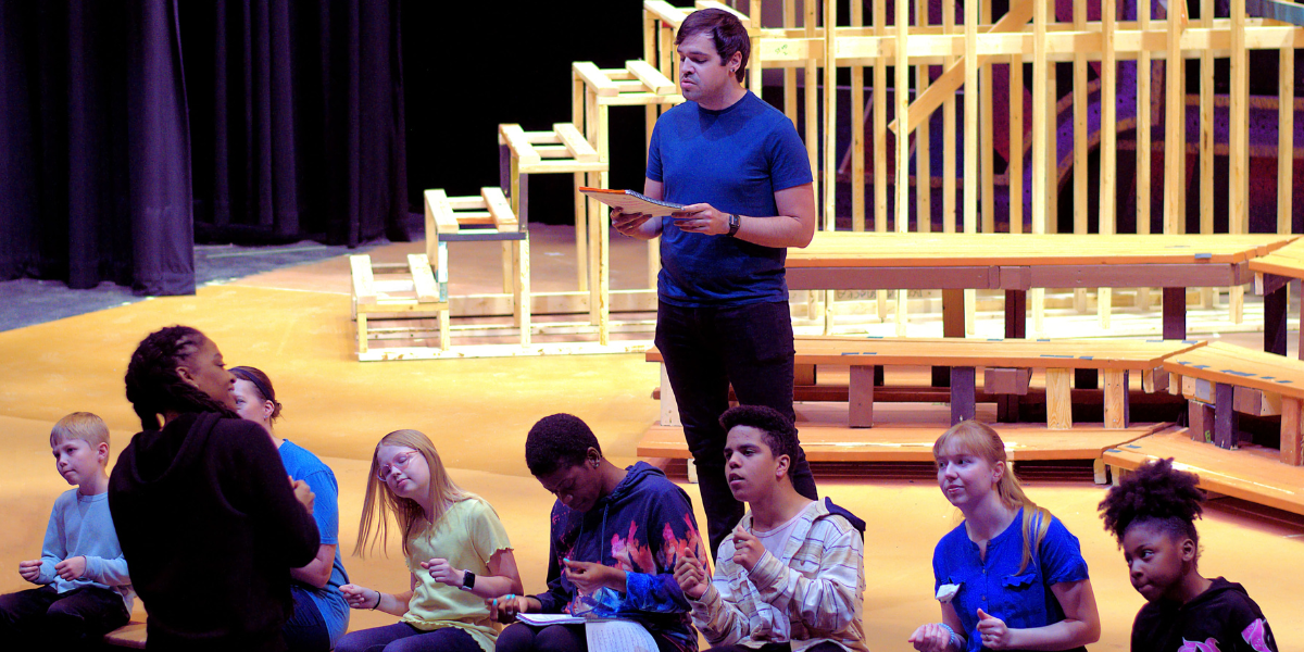 A man standing behind a row of sitting kids in a theater. 