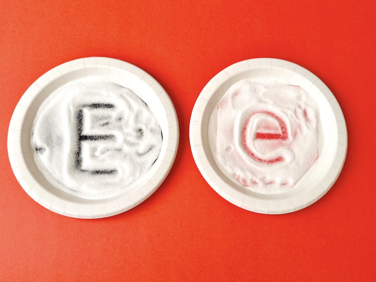 Two paper plates with salt on them, a large letter e outline on one and a small letter e outline on the other. 